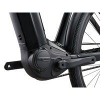 Close-up of a black mid-drive electric bike motor and crank on a matte frame, with the rear wheel visible in the background.