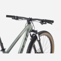 Close-up of a green Marin Marlin mountain bike front end, showing handlebars, grips, and front suspension fork with a knobby tire nearby