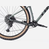 Close-up of a mountain bike's rear drivetrain: cassette, derailleur, chain, and crank on a gray frame with a tan-wall tire