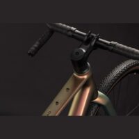 Close-up of a bronze-colored bicycle head tube and drop handlebars, with a section of the front tire visible against a dark background.