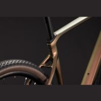 Close-up of a bronze bicycle frame near the rear wheel and seat post, highlighting the craftsmanship and geometry.
