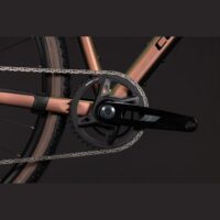 Close-up of a bicycle crankset with chainring and black crank arm on a copper frame against a dark background.