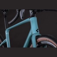 Close-up of a teal bicycle frame focusing on the head tube and front fork beside a brown-tired front wheel against a dark background.