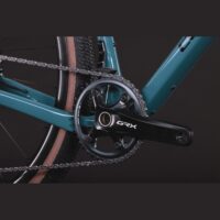 Close-up of a teal bicycle crankset and chainring labeled GRX, with the chain and rear tire visible.