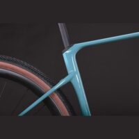 Close-up of turquoise bicycle frame and rear wheel with tan-wall tire against a dark background.