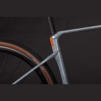 Close-up of a gray bicycle frame with an orange reflector and brown-tired rear wheel against a dark background.