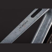 Close-up of a weathered metal beam with the brand name 'NUROAD' and a black rubber strip along its edge.