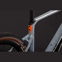 Close-up of a silver bicycle frame with an orange accent near the seat post and a portion of the rear wheel.