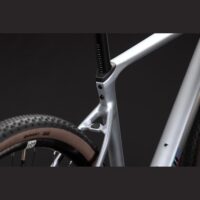 Close-up of a silver bicycle frame around the seat tube and rear triangle, with a black seatpost and tan-walled tire visible.