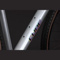 Close-up of a silver bicycle frame tube with a colorful CUBE logo and a knobby tire visible on the right.