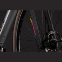 Close-up of a bicycle front fork with a colorful vertical stripe sticker, front wheel and disc brake visible against a dark background.