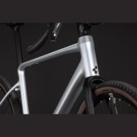 Close-up of a silver bicycle frame with a black front fork and tan-walled tires, logo on head tube visible.
