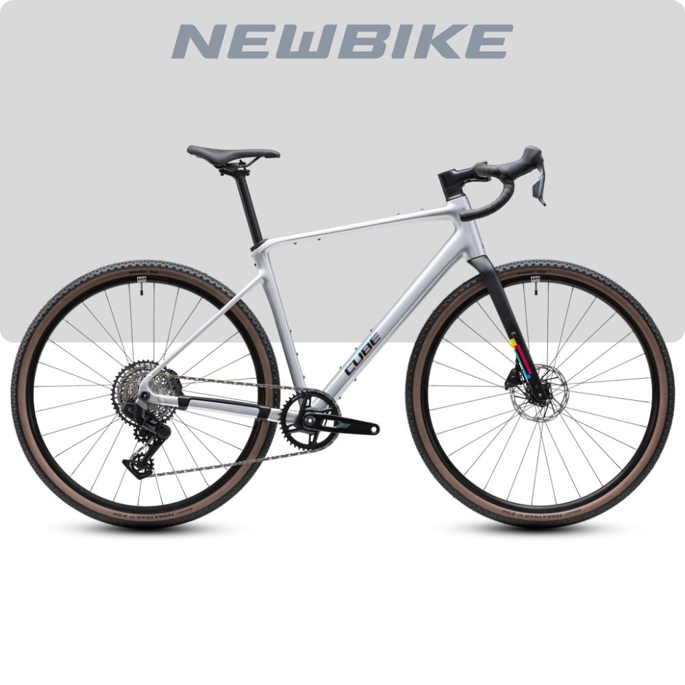 Silver NewBike gravel bike with drop handlebars, 1x drivetrain, and tan-wall tires, shown against a light gray background